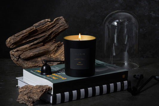 Wild Musk lit candle on a set of books with black snuffer, wick cutter and glass dome on a dark grey background