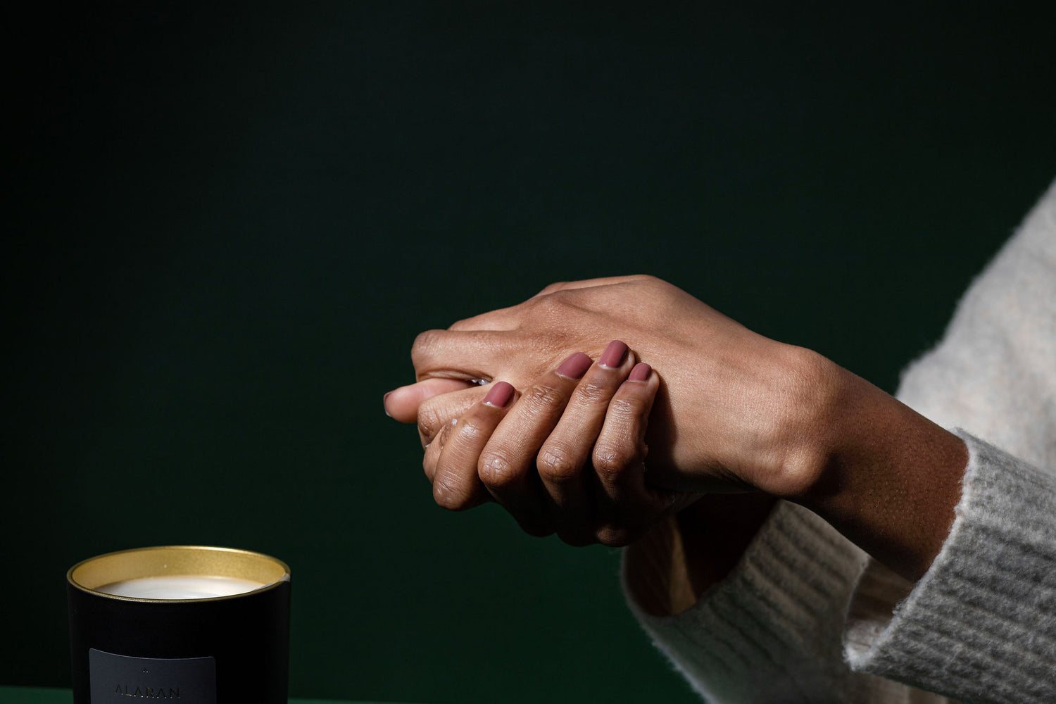 Hands being rubbed together next to candle on a dark green background