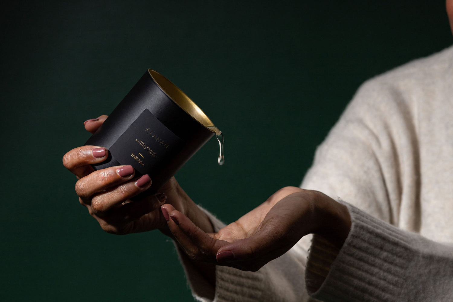Wild Musk Candle being poured into hand on a dark green background